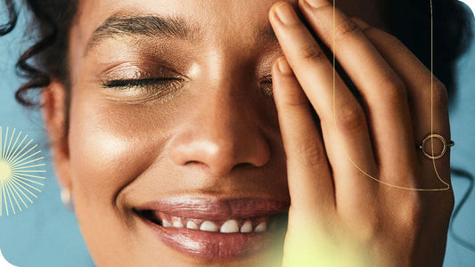 mulher com os olhos fechados e sorrindo, com uma das mãos cobrindo metade do seu rosto